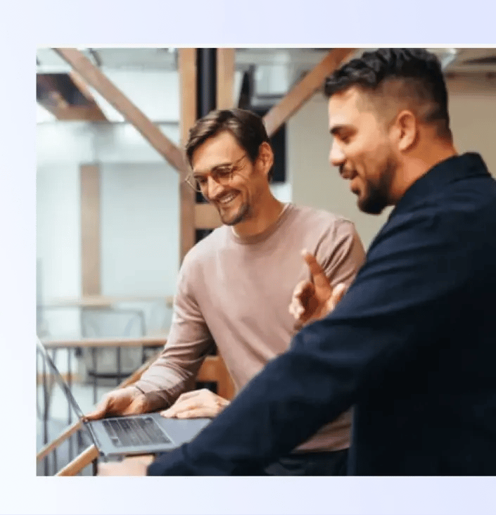 Two men engage in a discussion while examining a laptop.